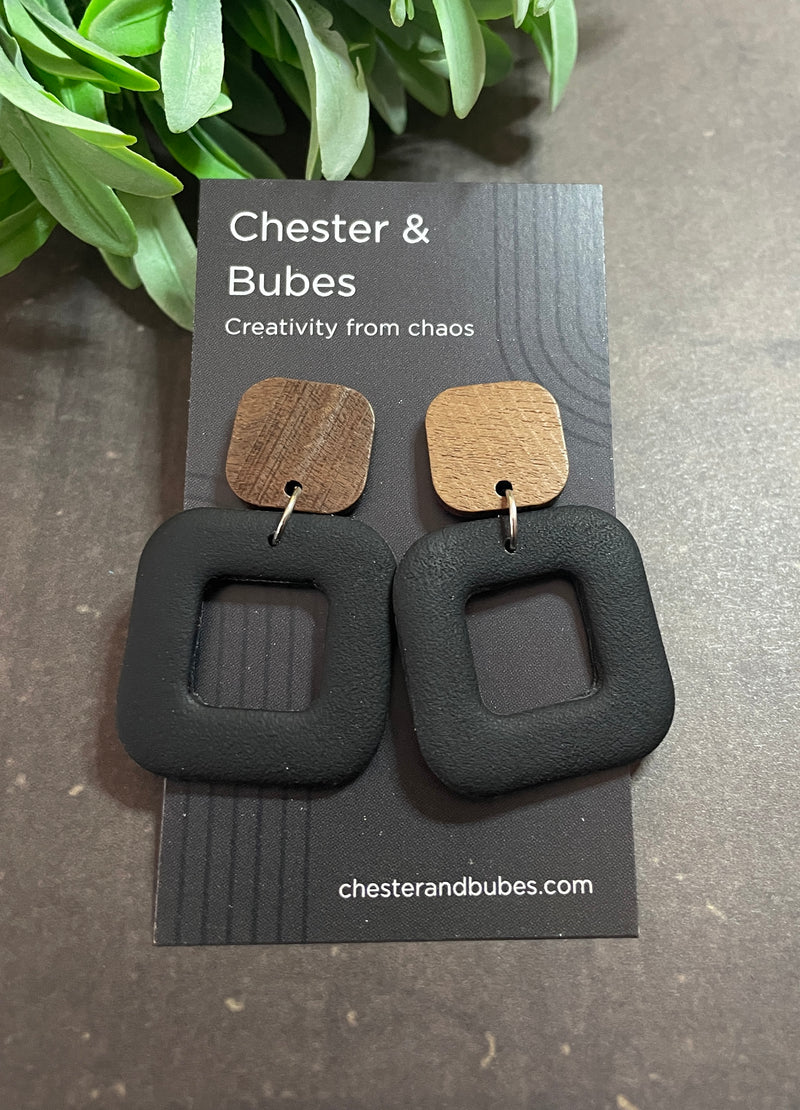Pair of chunky black earrings with a wooden topper on a 'Chester & Bubes' branded card with green leaves in the background.