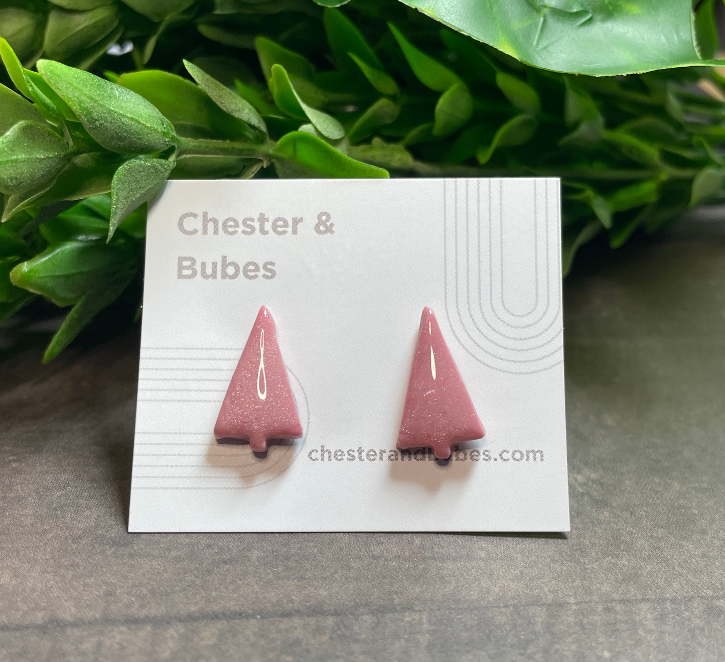 Pink Christmas tree earrings on a 'Chester & Bubes' branded card with green leaves in the background.