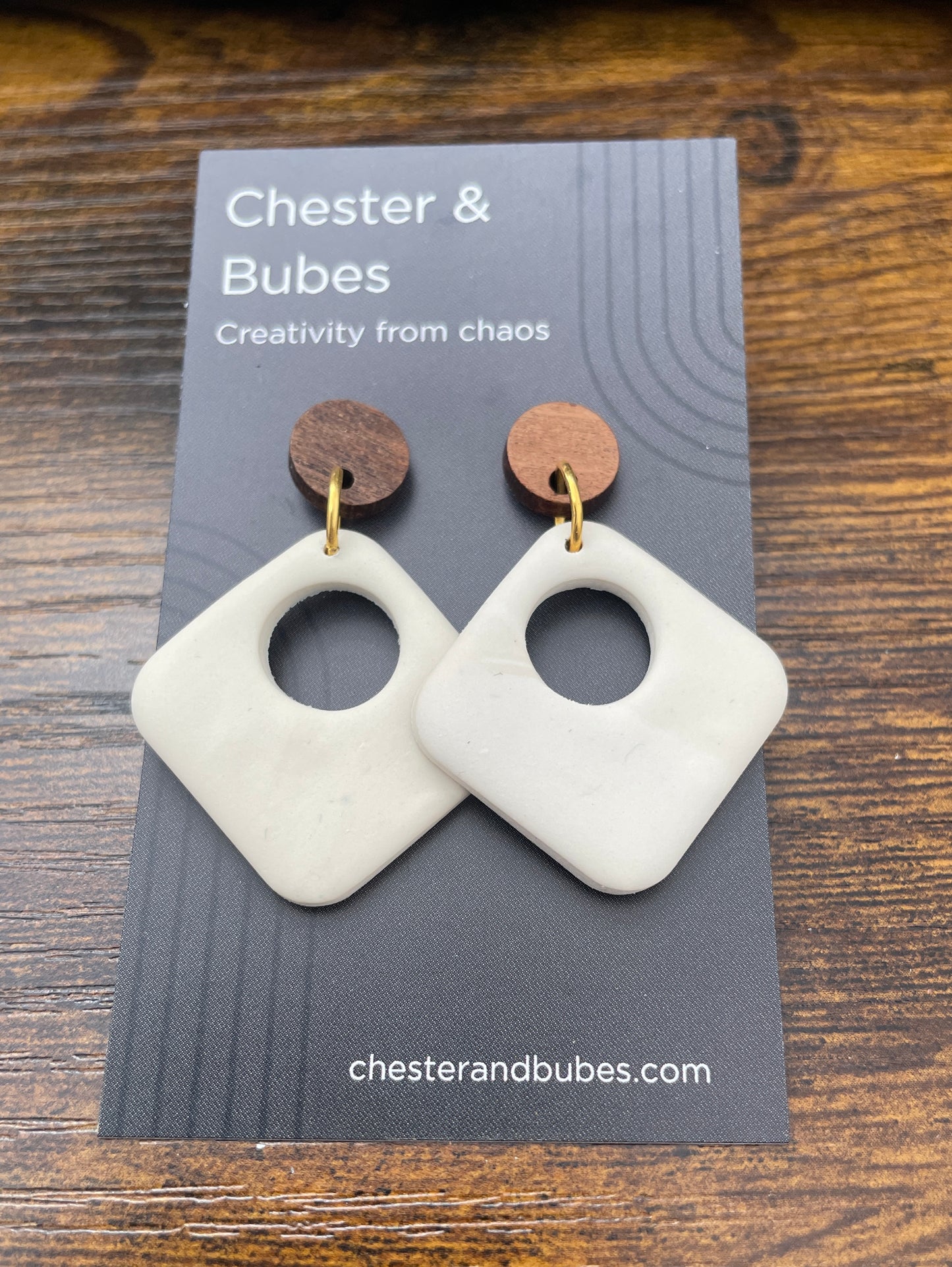 White geometric earrings on a 'Chester & Bubes' branded card with a wooden background.