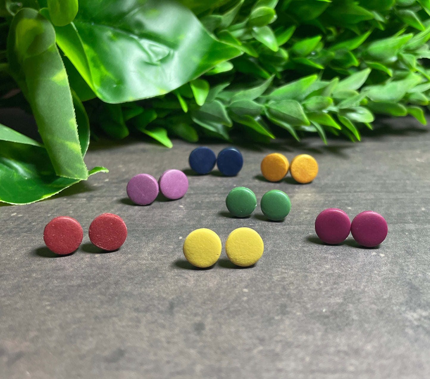 Set of rich coloured round earrings on a gray surface with green leaves in the background