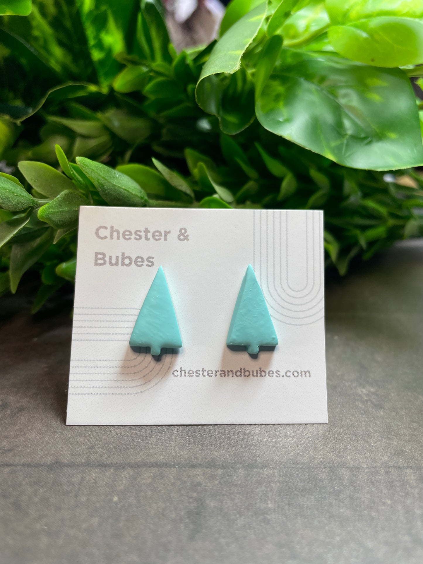 Turquoise earrings on a white card with 'Chester & Bubes' branding, against a green leafy background.
