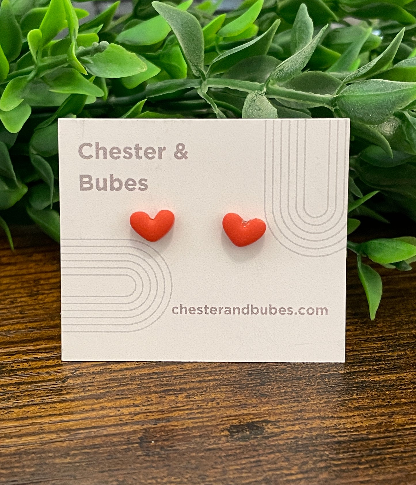 Orange heart-shaped earrings on a 'Chester & Bubes' branded card with green leaves in the background.