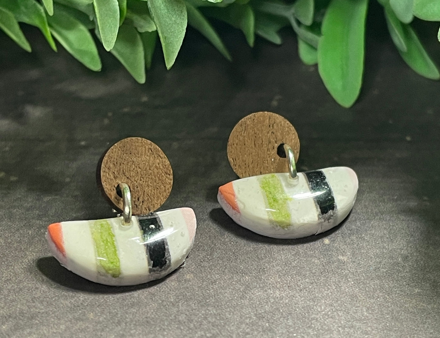 Pair of earrings with striped design on a dark surface with green leaves in the background