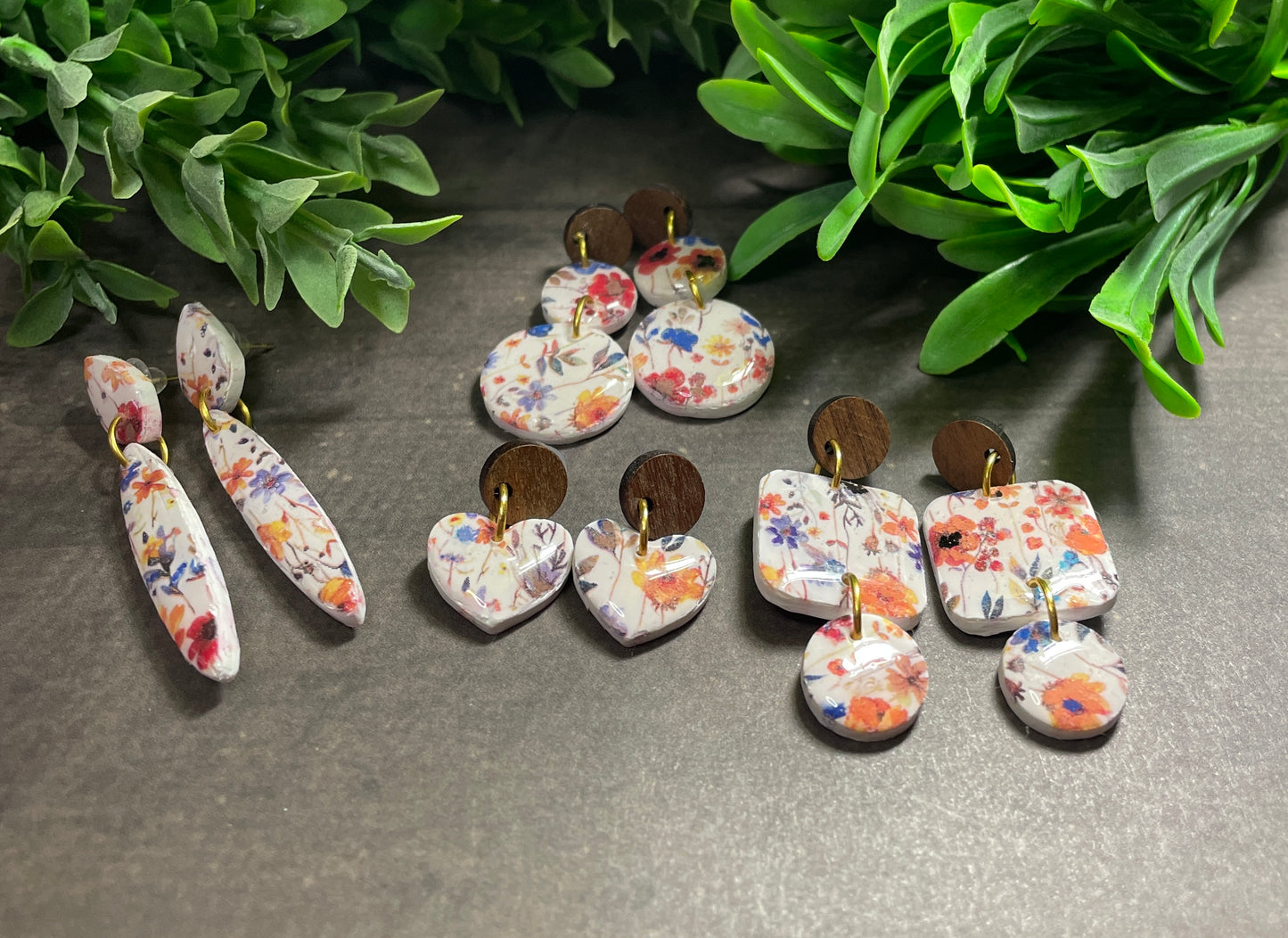 Set of floral earrings on a dark surface with green leaves in the background