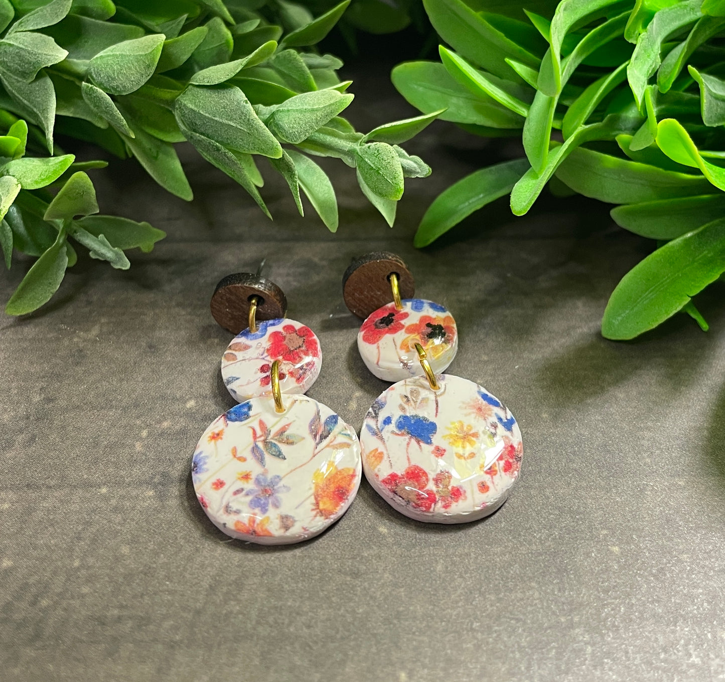 Pair of floral earrings on a gray surface with green leaves in the background