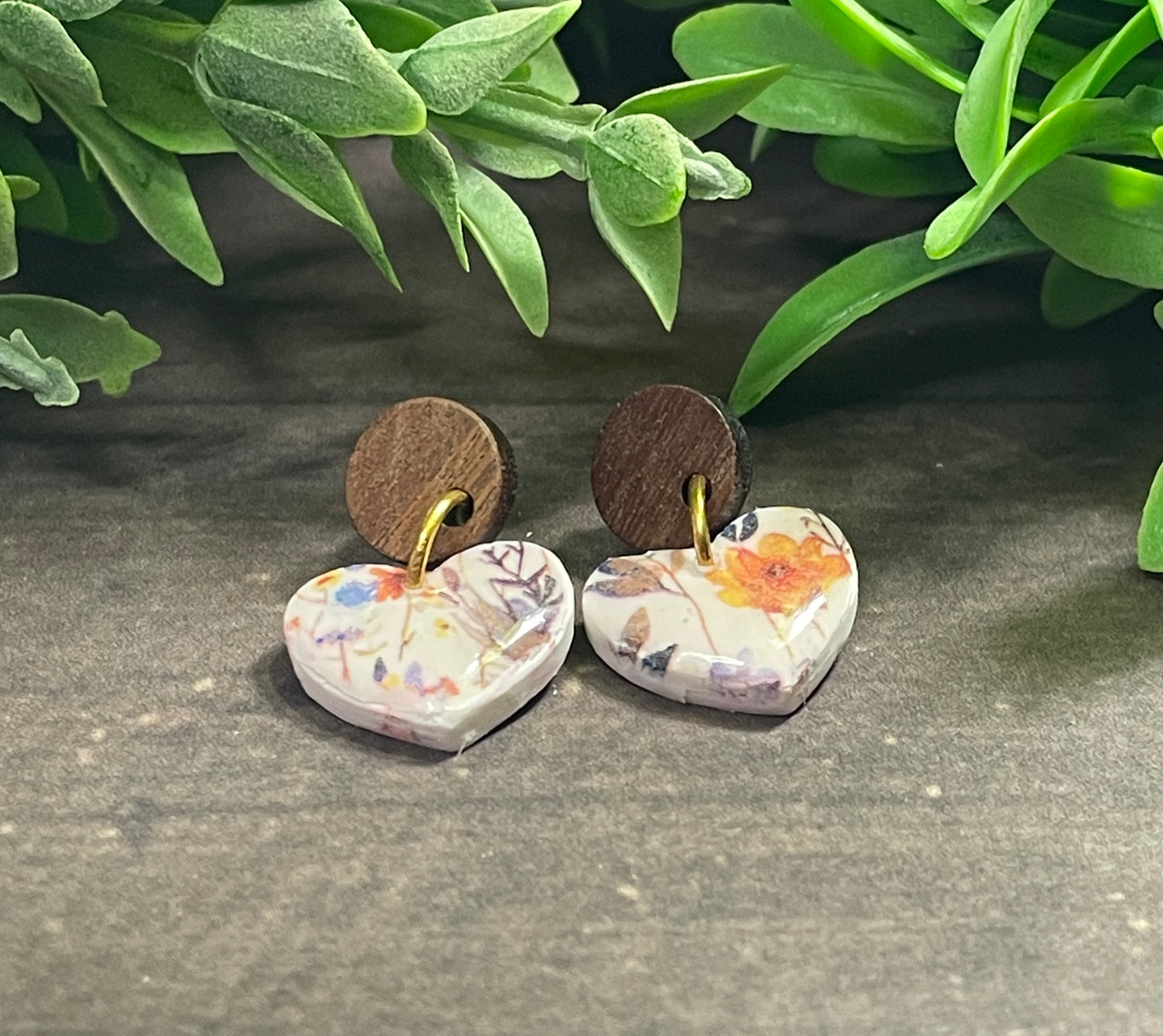 Heart-shaped earrings with floral patterns on a gray surface with green leaves in the background