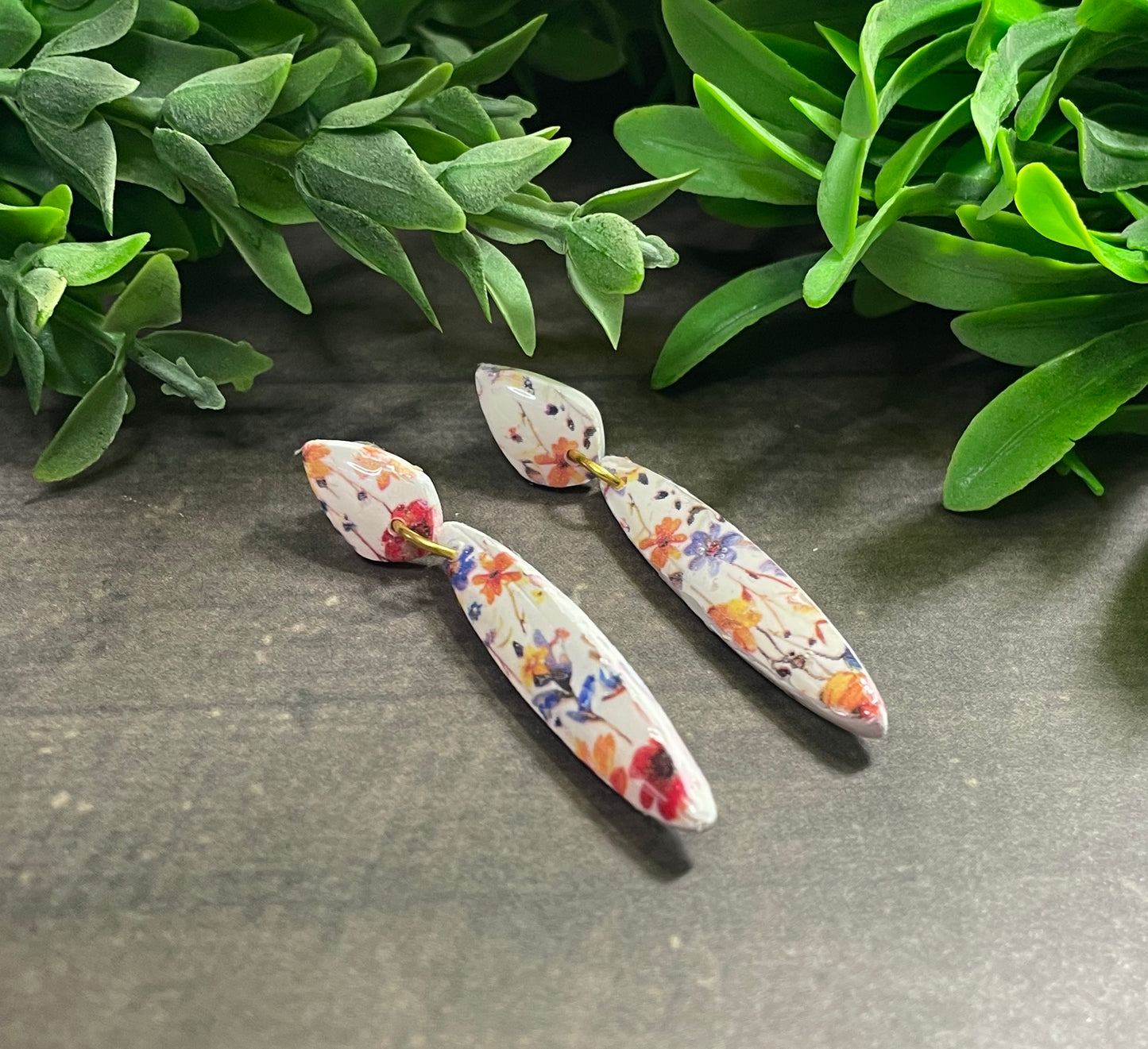 Floral patterned earrings on a gray surface with green leaves in the background
