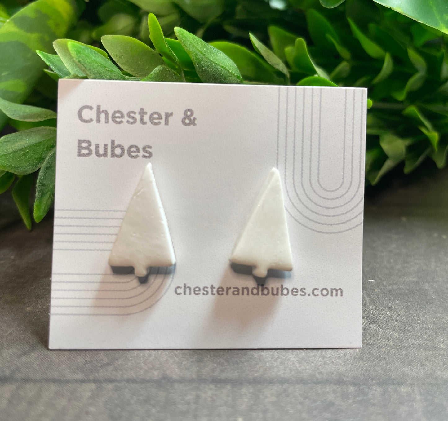 White Christmas tree earrings on a 'Chester & Bubes' branded card with green leaves in the background