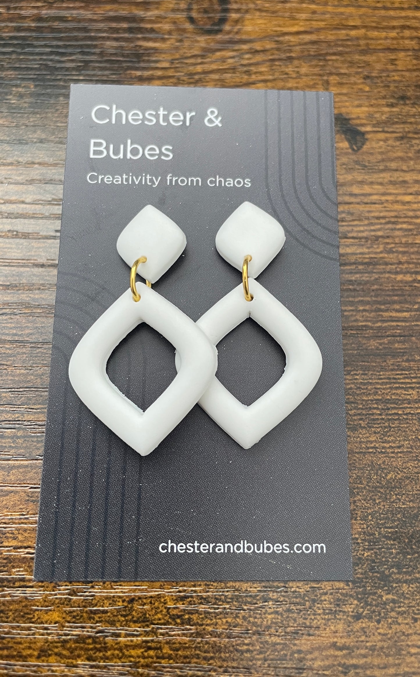 White earrings on a 'Chester & Bubes' branded card with a wooden background