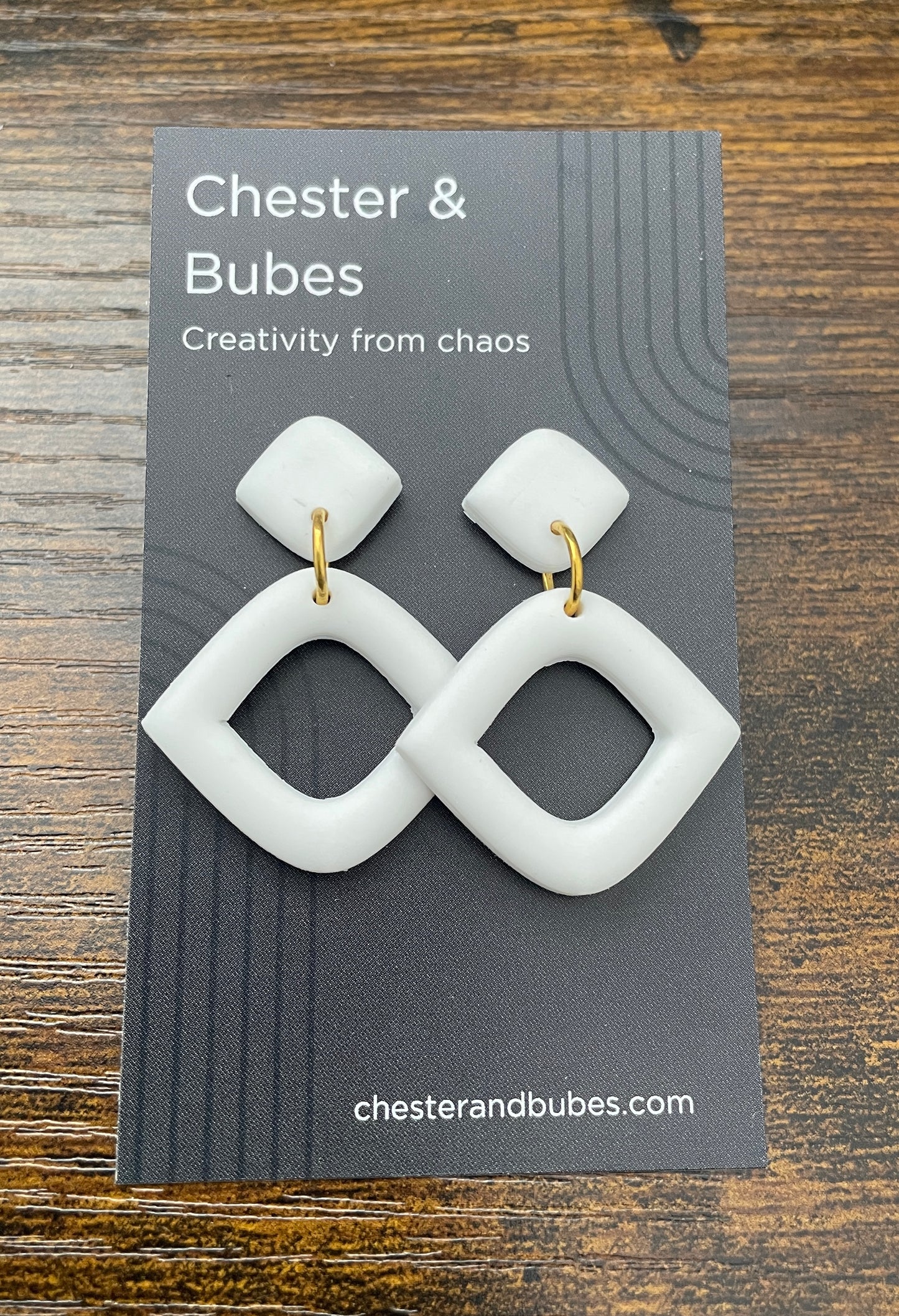 White earrings on a Chester & Bubes branded card with a wooden background
