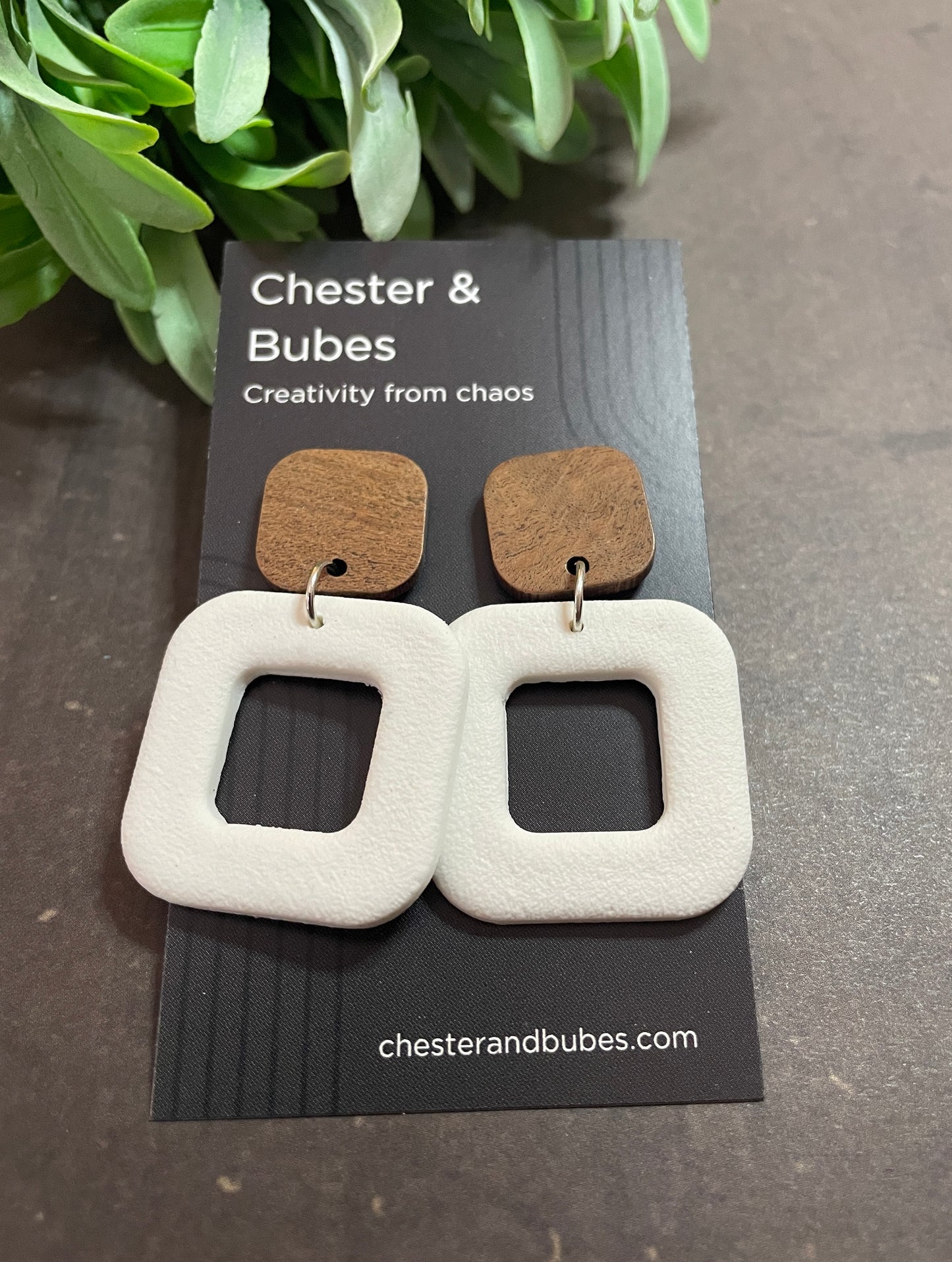 Pair of chunky white earrings on a Chester & Bubes card with greenery in the background