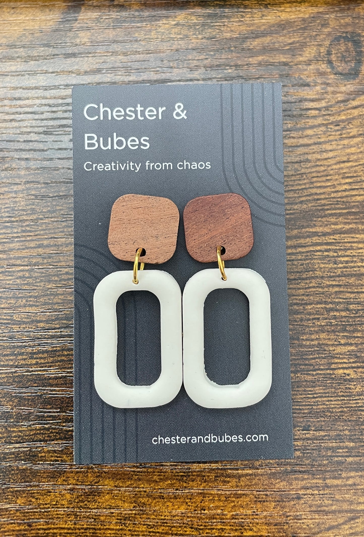Wooden and white earrings on a 'Chester & Bubes' branded card against a wooden background