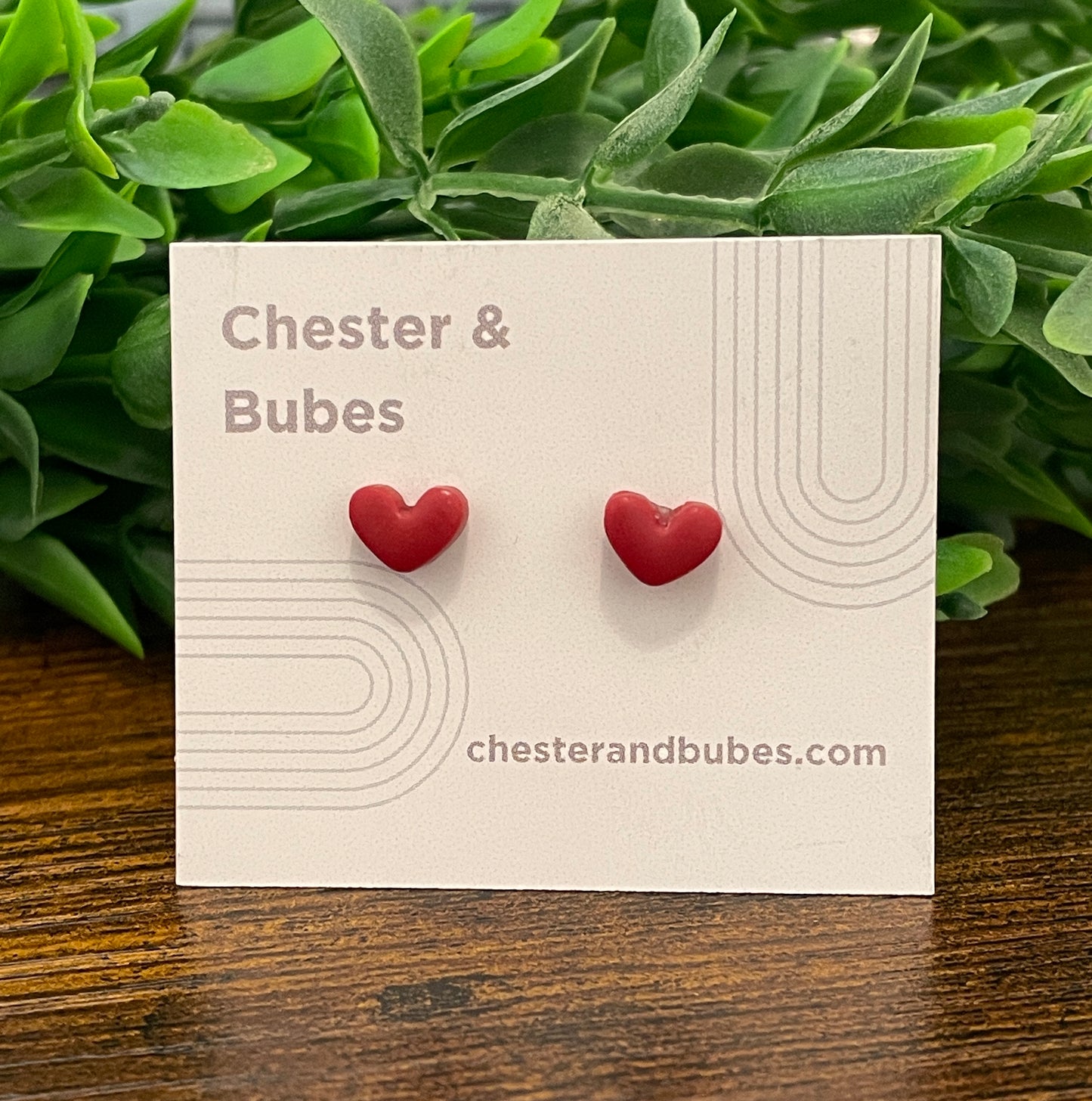 Cranberry red heart-shaped earrings on a 'Chester & Bubes' branded card with green leaves in the background.