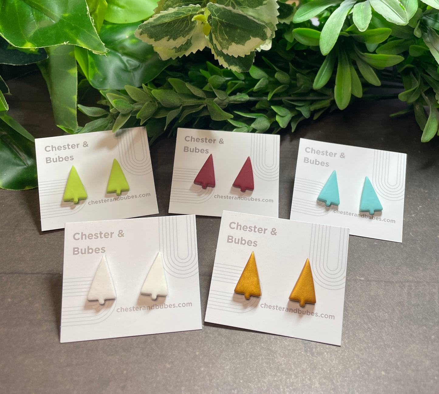 Set of  Christmas tree stud earrings on display with their packaging against a green leafy background