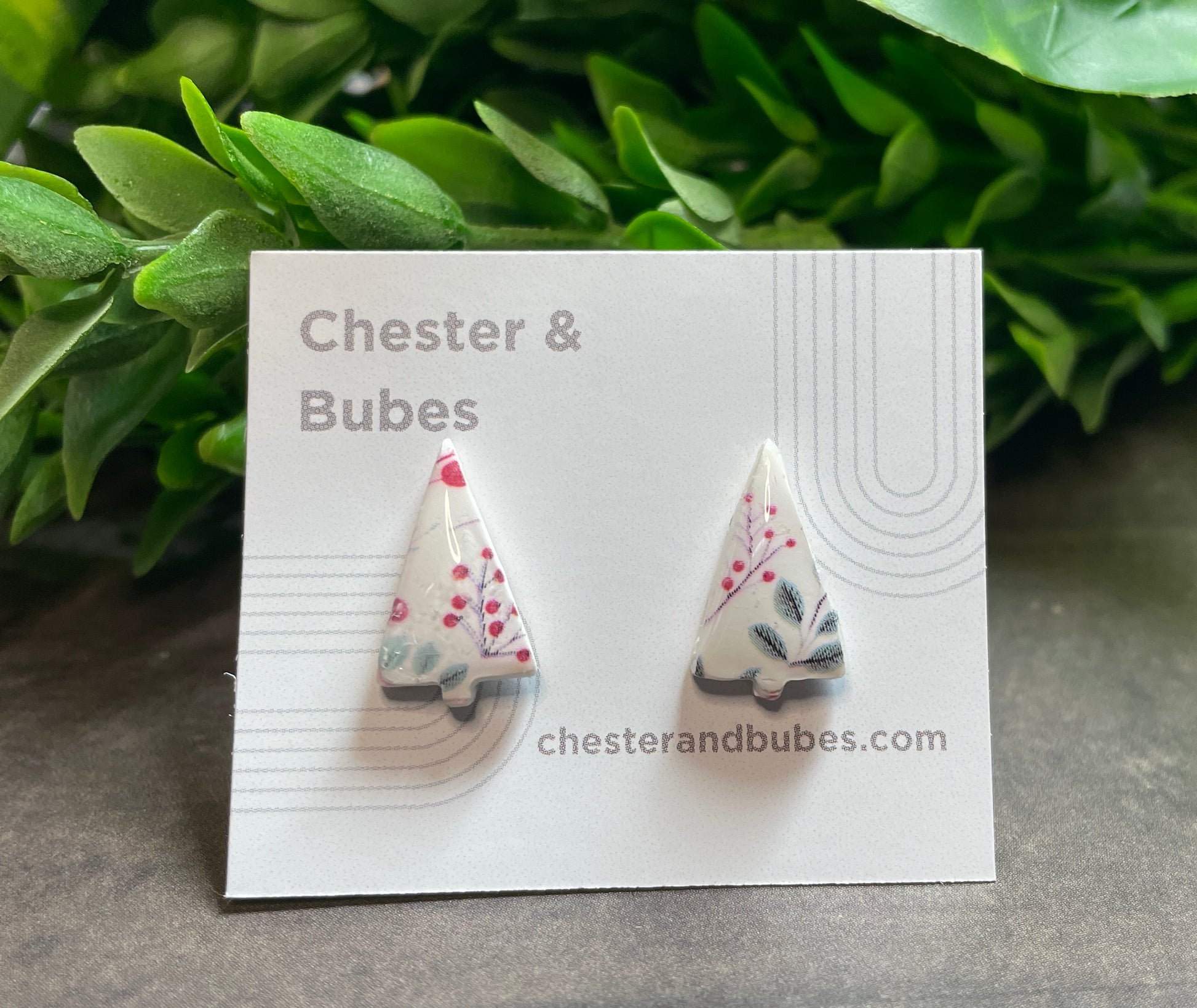 Festive pattern Christmas tree earrings on a 'Chester & Bubes' branded card with green leaves in the background