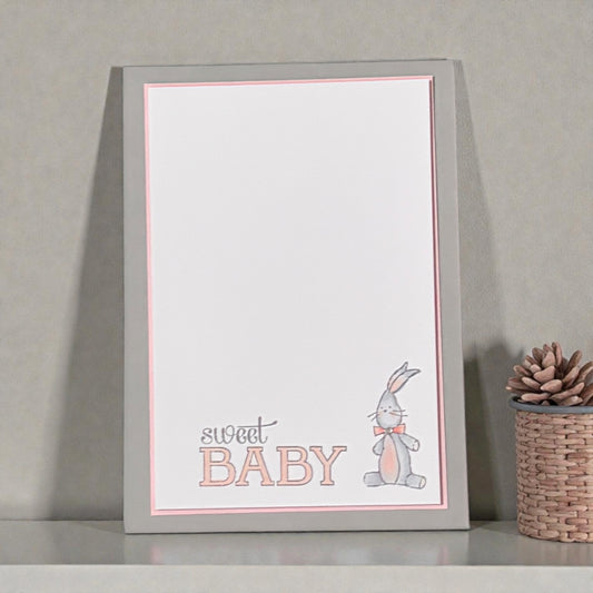 New baby card with a bunny illustration on a gray surface.