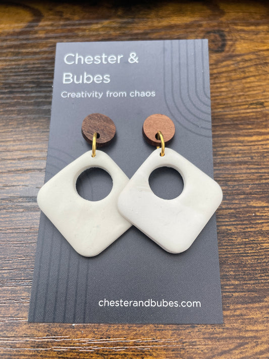 White geometric earrings on a 'Chester & Bubes' branded card with a wooden background.