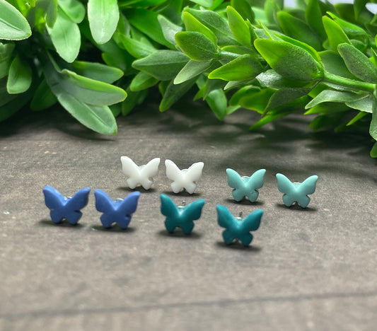 Butterfly-shaped earrings in blue and white on a textured surface with green leaves in the background