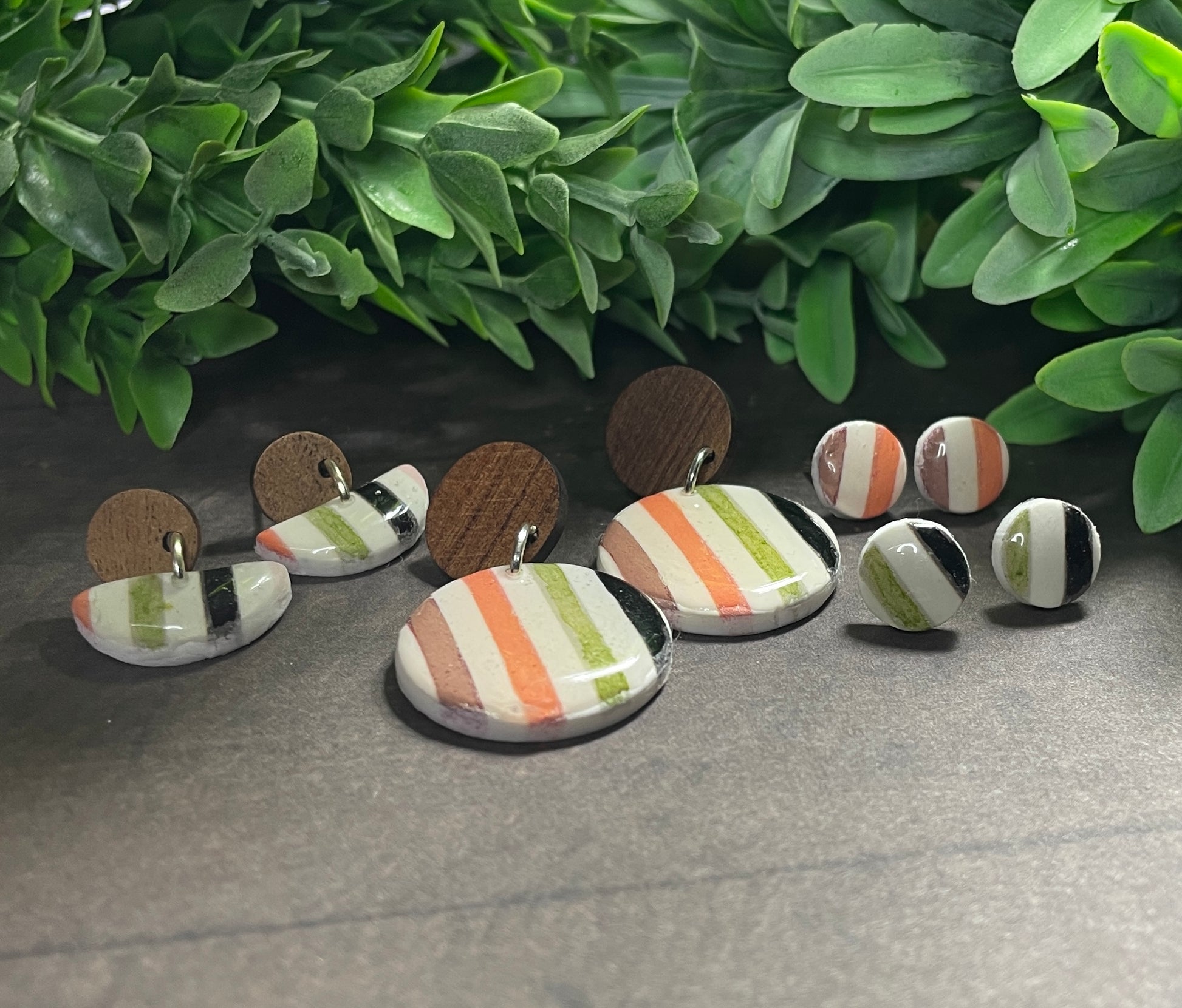 Set of earrings with striped patterns on a gray surface with green leaves in the background