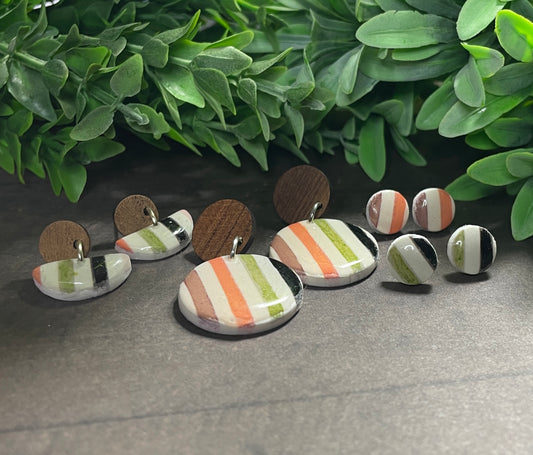 Set of earrings with striped patterns on a gray surface with green leaves in the background