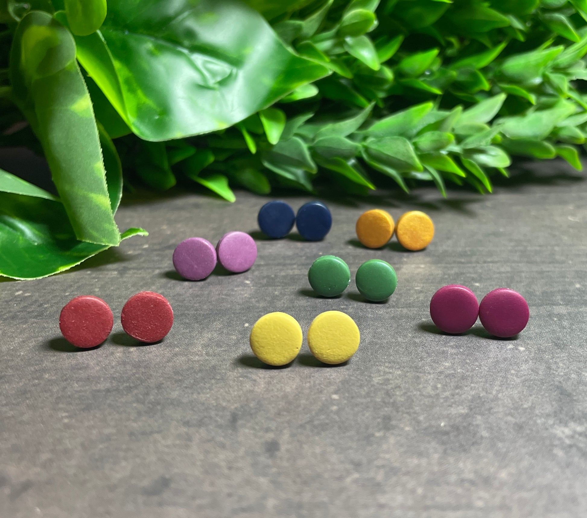 Set of rich coloured round earrings on a gray surface with green leaves in the background