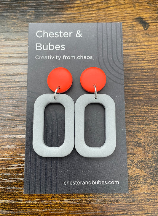 Earrings with a bright orange copper with a grey squoval cutout shape. 