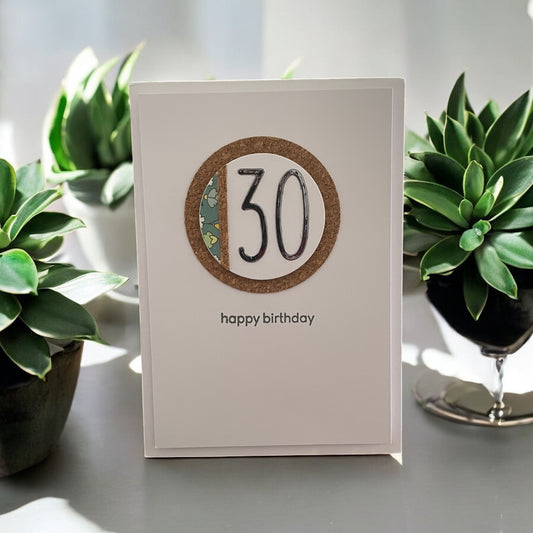 White birthday card with '30' and 'happy birthday' text, surrounded by green plants.