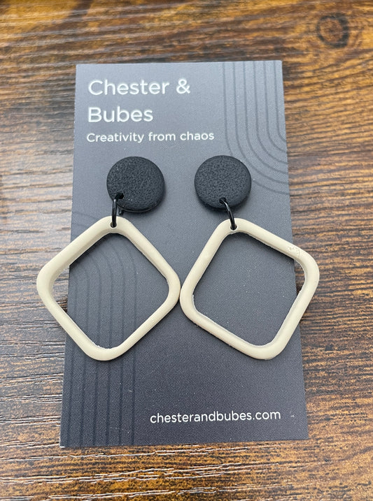 Pair of earrings on a 'Chester & Bubes' branded card.  Earrings have a textured black round topper, approx 1.5 cm diameter with a cream coloured offset cutout square. 