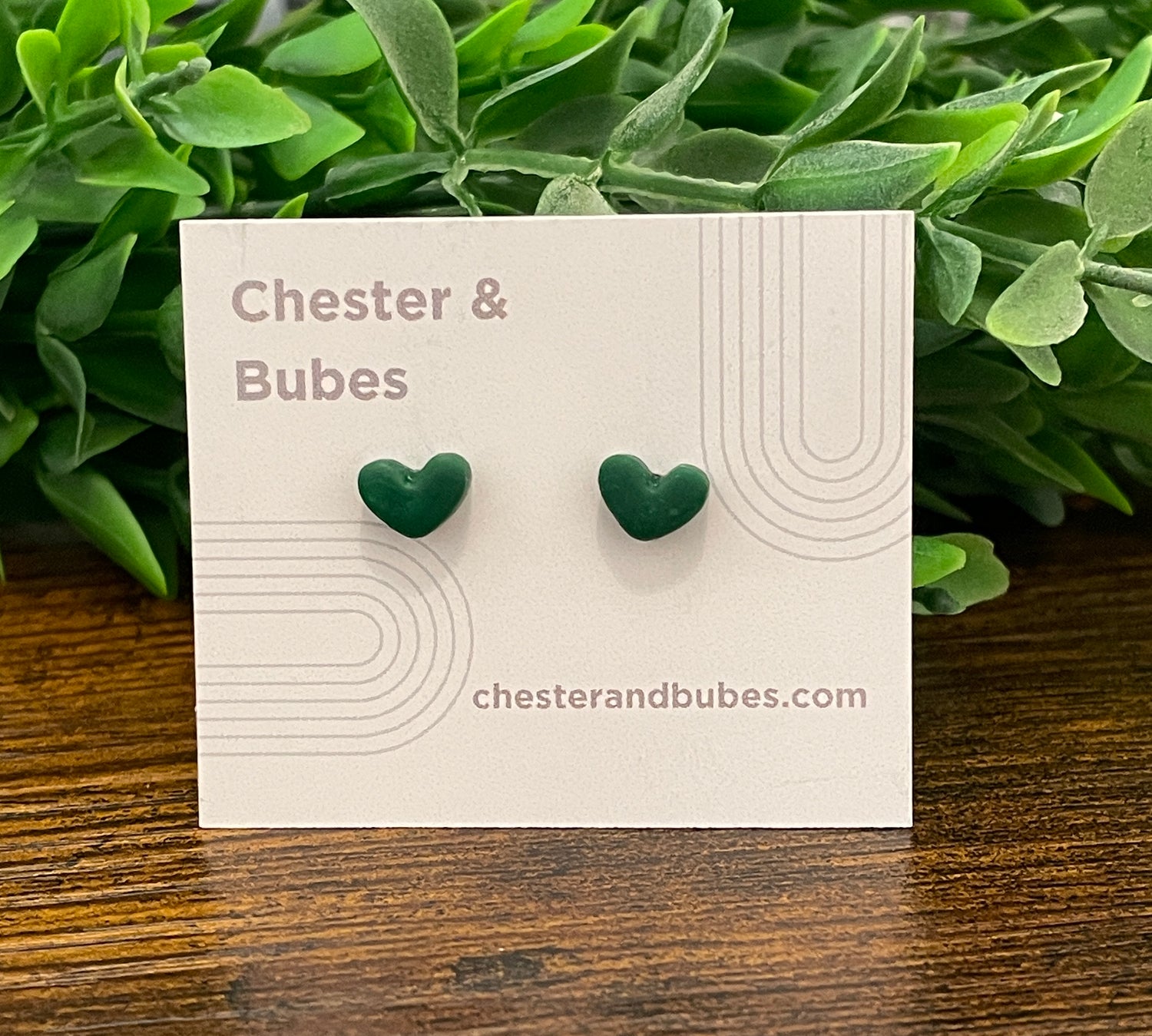 Green heart-shaped earrings on a Chester & Bubes branded card with green leaves in the background
